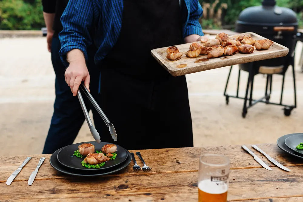 Grilled bites being served onto plates at a long outdoor table